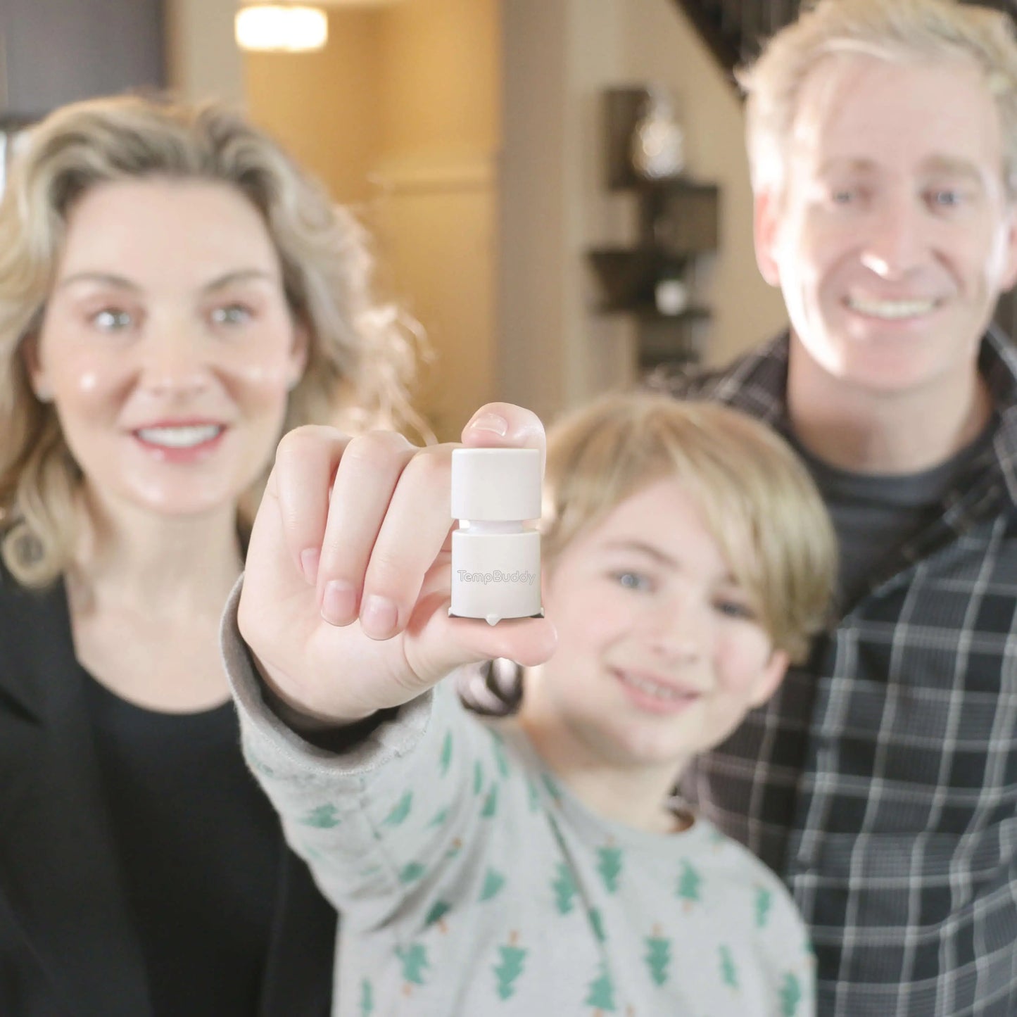 A smiling family of three, with their young son in the foreground holding up the TempBuddy smart thermometer.