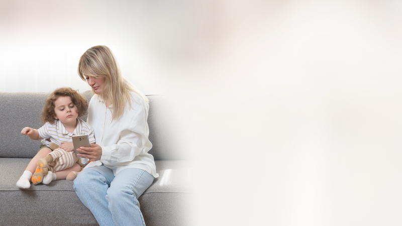 A parent and young child sitting together on a sofa, looking at a phone