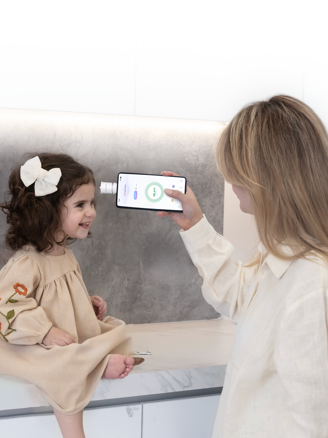A parent scanning a child's forehead with TempBuddy plugged into a phone