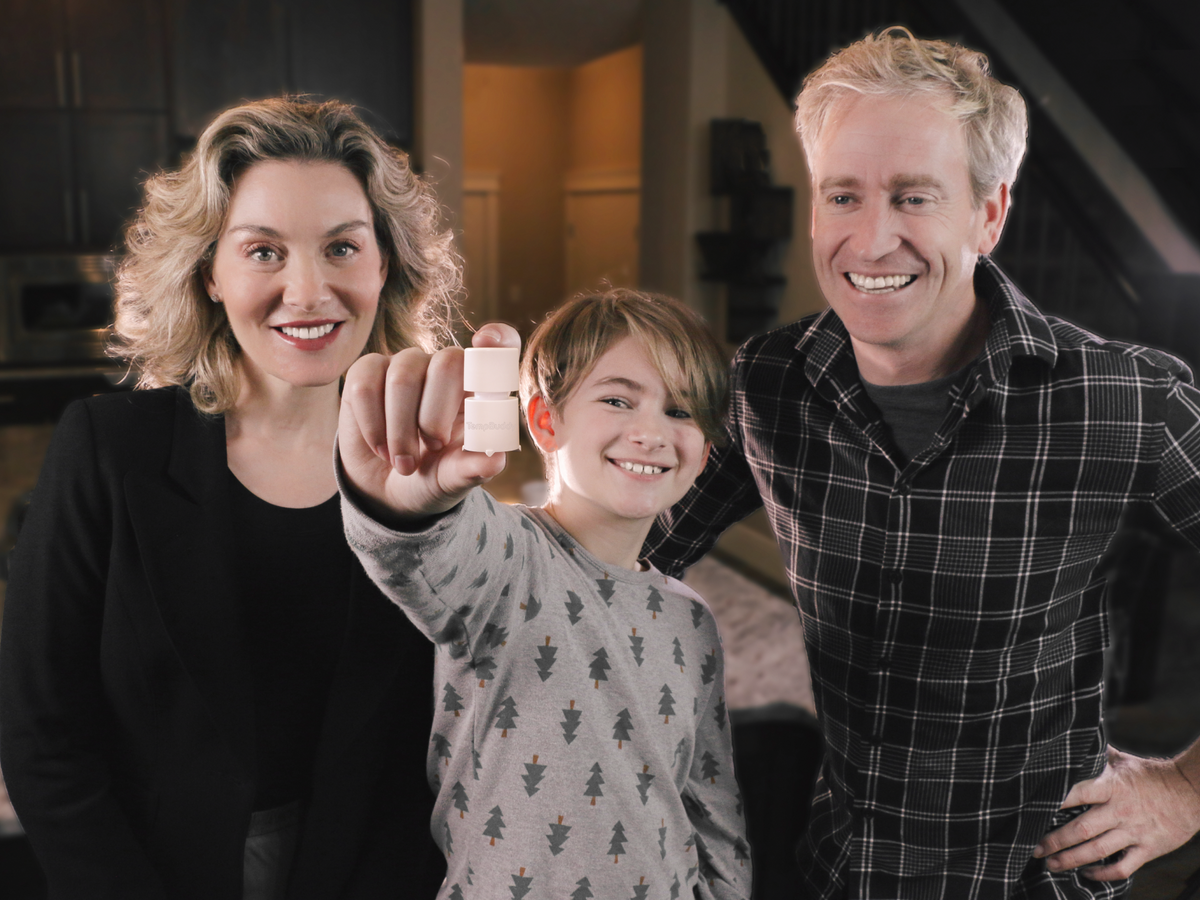 A family holding up a TempBuddy device at home