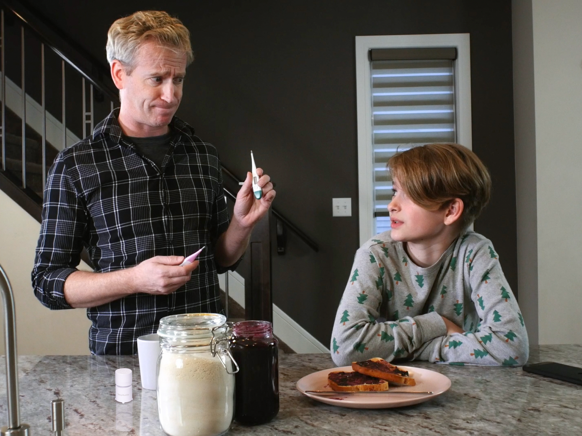 A father holding two old thermometers while his son looks on unimpressed